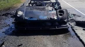 An image of a burned up Noble M400 on the side of the road.