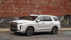 A white 2023 Hyundai Palisade parked next to a brick wall. This is one of many Hyundai SUVs.
