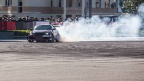 A Nissan drift car slides in a cloud of smoke in front of spectators.