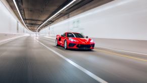 A red C8 Corvette speeding through a tunnel under overhead lights.