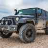 Dark colored Jeep Wrangler with a snorkel parked on desert sands in low left front angle view